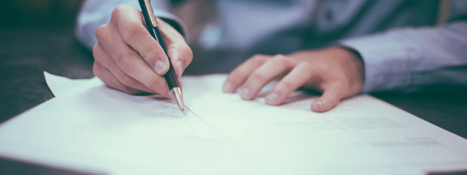 Person signing business documents with a pen representing contracts and terms